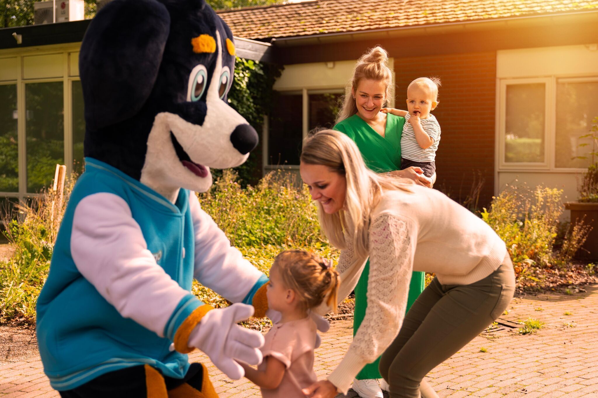 A mascot interacting with a family in a garden setting.