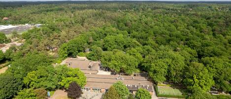 An aerial view of a residential area with a large building, surrounded by dense forest.