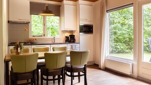 Una cocina moderna con armarios blancos, una mesa de comedor con cuatro sillas, una lámpara colgante y vistas a la vegetación a través de grandes ventanales.