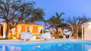 A poolside area with lounge chairs, a dining setup, and a large tree. - 4 Bedroom Villa in Pozzallo (Pozzallo)