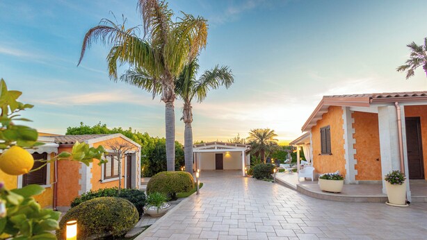 A pathway leading to a building with a covered entrance, surrounded by well-maintained hedges and palm trees. - 4 Bedroom Villa in Pozzallo (Pozzallo)