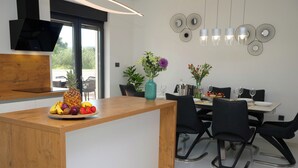 A modern kitchen with a wooden island, fruit bowl, and dining area with chairs and a table. - Villa Golden Shine with heated pool, Primošten (Primošten)