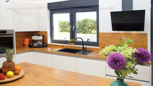 A modern kitchen with white cabinets, a wooden countertop, a black sink, and a window with a view of greenery. - Villa Golden Shine with heated pool, Primošten (Primošten)