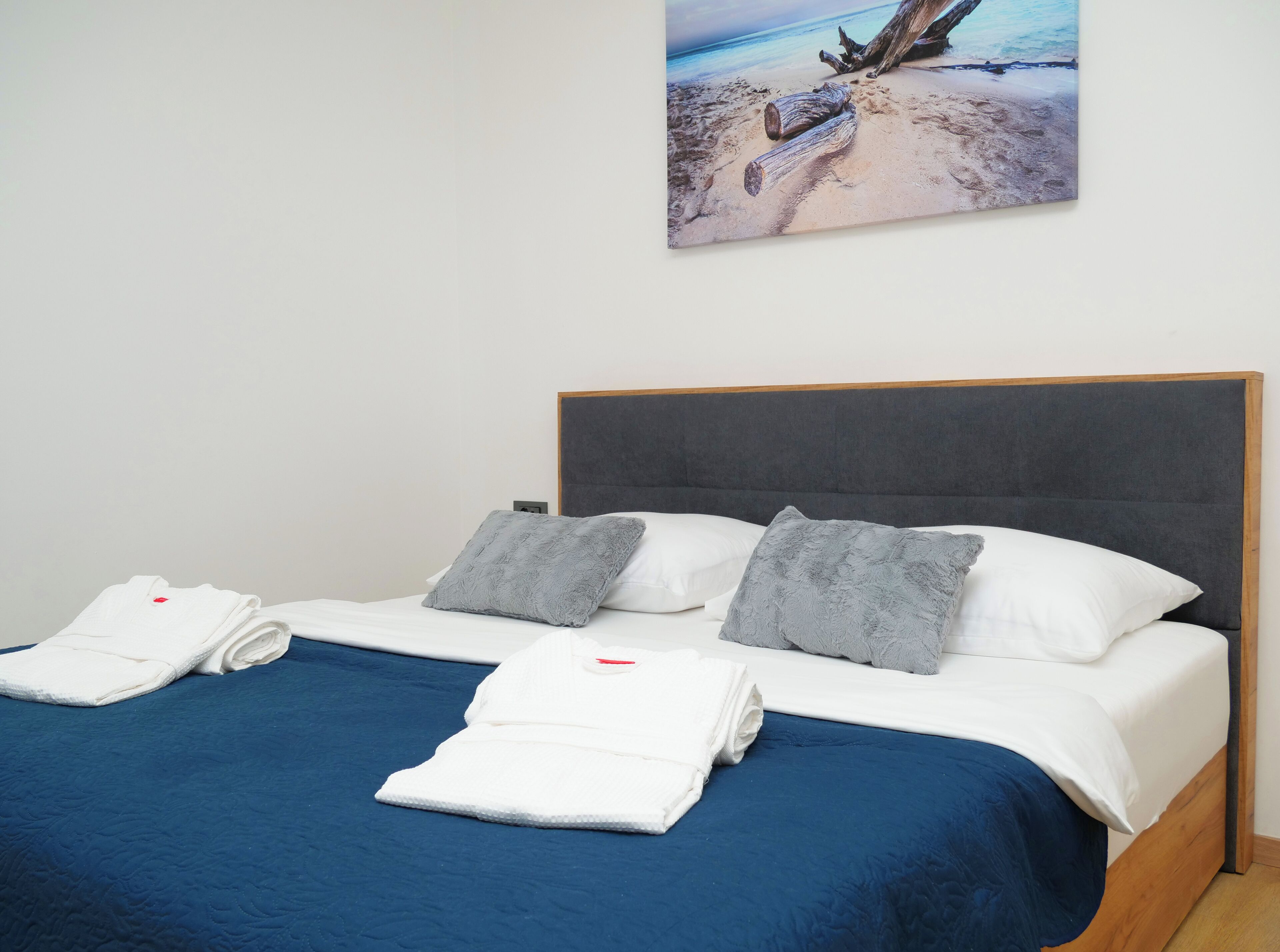 Un lit avec une tête de lit sombre, deux oreillers et une couvre-lit bleue.