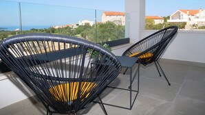 A balcony with two black wicker chairs and a table, overlooking a coastal area with buildings and greenery. - Villa Golden Shine with heated pool, Primošten (Primošten)