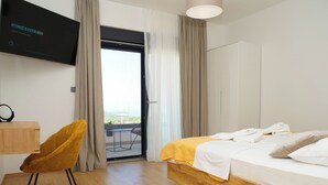 A hotel room with a bed, a wooden desk, a chair, a TV, and a balcony with a table and chairs. - Villa Golden Shine with heated pool, Primošten (Primošten)