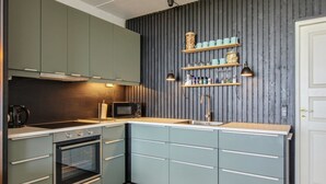 Uma cozinha compacta com micro-ondas, forno e pia. Há prateleiras de madeira acima da pia e uma porta à direita.
