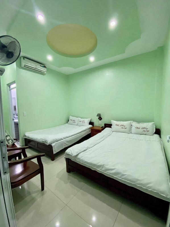 A room with two single beds, a wooden chair, a desk, and a ceiling fan.