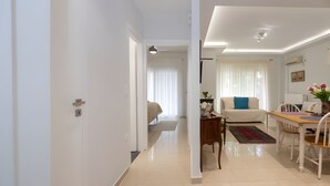 Uma sala moderna com sofá, mesa de jantar e cadeiras. Há um corredor que leva a um quarto com cama.