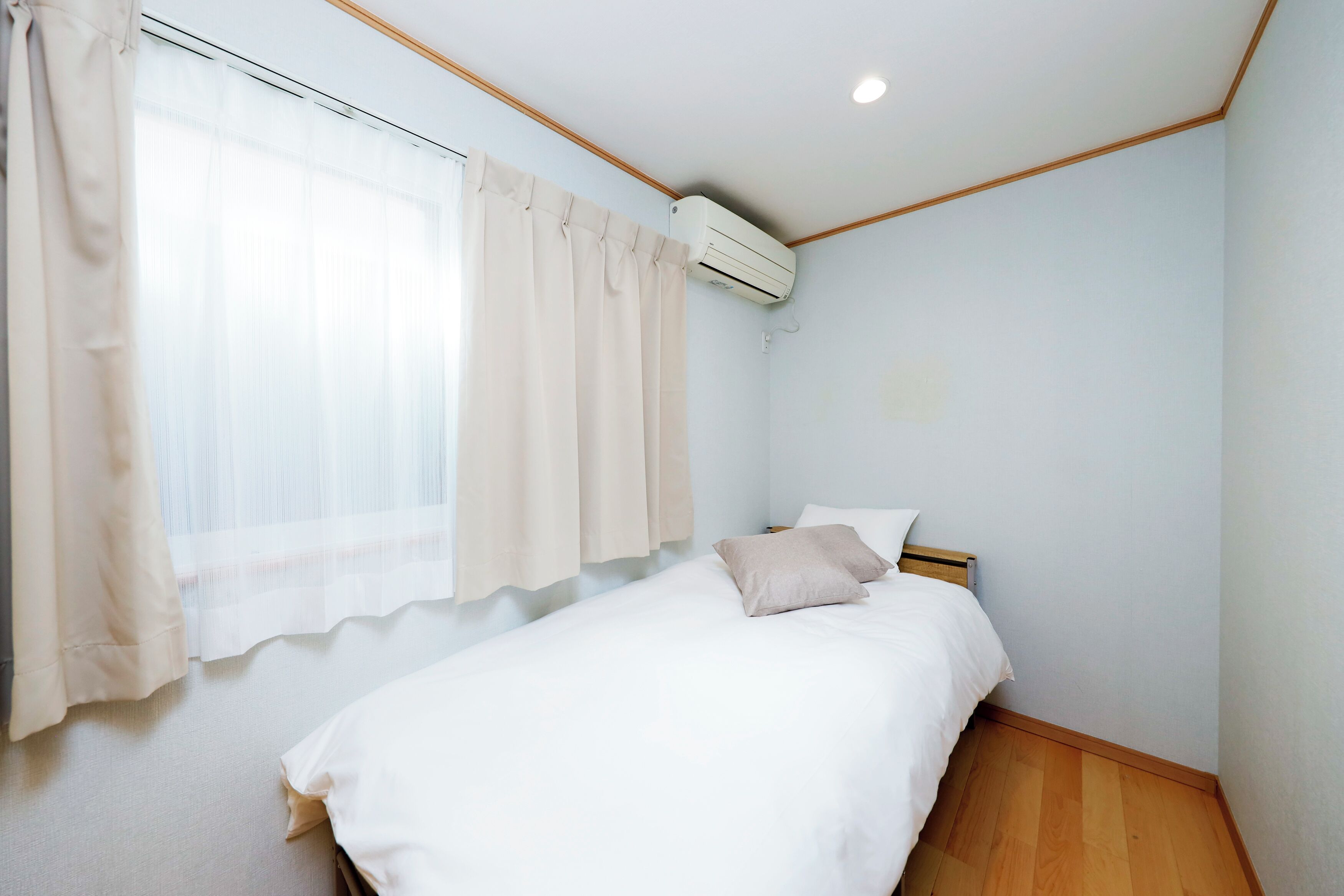 A bedroom with a bed, beige curtains, an air conditioning unit, and wooden flooring.