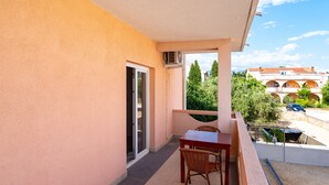 A balcony with a table and chairs, a sliding glass door, and a view of a building with arches and trees. - Bonvie Apartments in Center 12 B6 (Novalja)