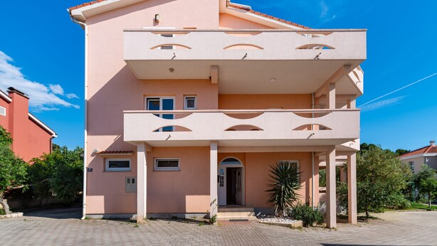 A two-story building with a balcony, a small entrance, and a visible door. - Bonvie Apartments in Center 12 B6 (Novalja)
