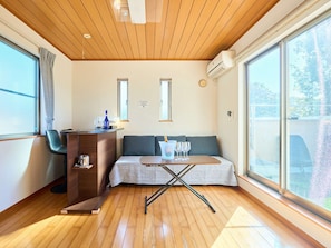 A modern room with a wooden ceiling, a sofa, a small table, a desk with a chair, and large windows. - Quality lodging in the heart of Tokyo. A 4-minute walk from Tabata Station on the JR Yamanote Line. Maximum of 19 people. (北区)