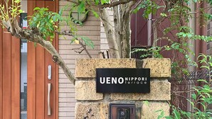 A stone wall with a sign reading "UENO NIPPORI terrace" and a security camera mounted on it.