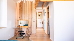 A modern room with a wooden slat wall, a desk with a mirror, a small bathroom, and a wooden floor.