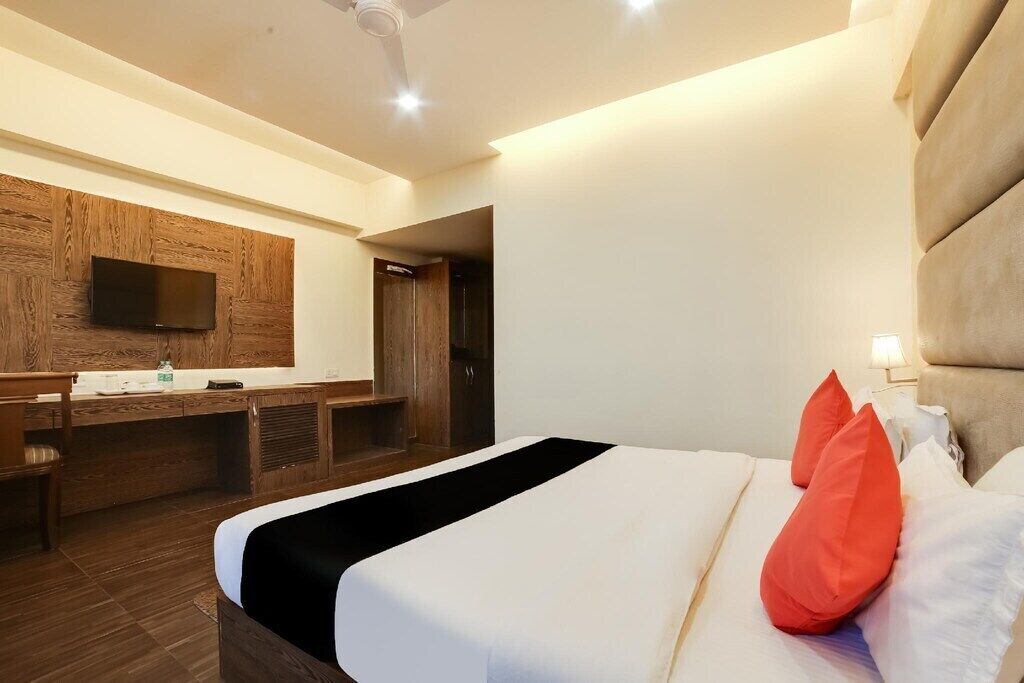 Ein Hotelzimmer mit Bett, Fernseher an einer Wand aus Holzpaneelen, Schreibtisch mit Stuhl und Badezimmertür.