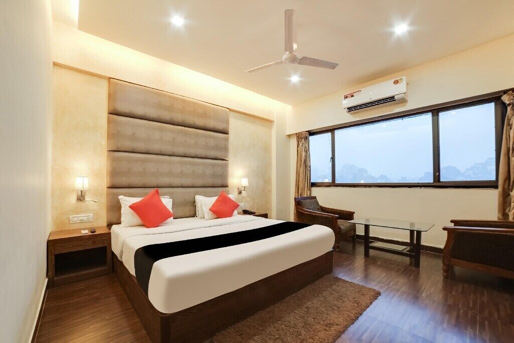 A modern hotel room with a large bed, a desk, a chair, a ceiling fan, and a large window with a view.