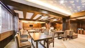 Un'ampia sala da pranzo con tavoli di legno e sedie a righe, un soffitto decorato con motivi nuvolosi e una parete in legno rustico.