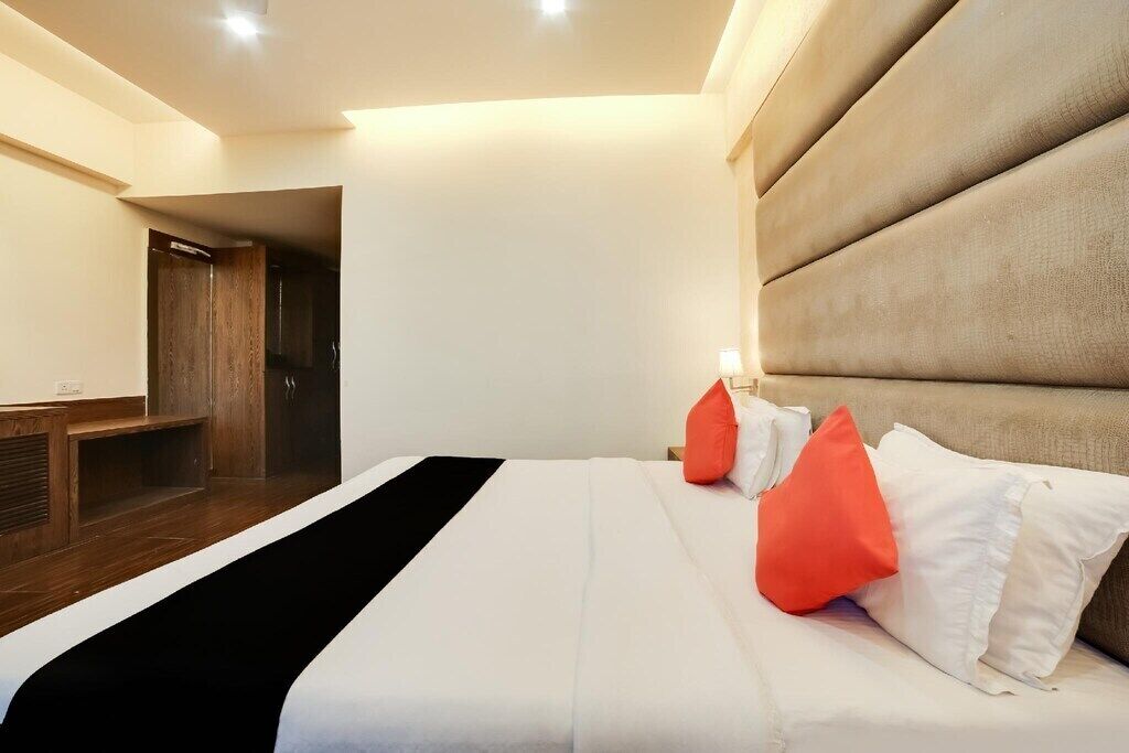 A hotel room with a large bed, a wooden bench, and a headboard with built-in lighting.