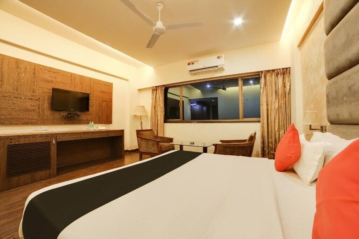 A hotel room with a bed, a desk, a TV, and a window with curtains.