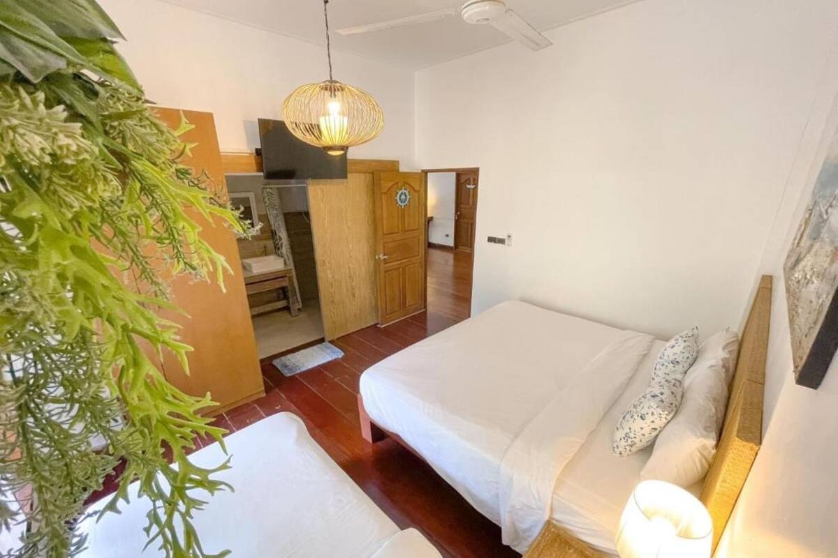 A room with two beds, a wooden floor, a hanging light fixture, and a plant.