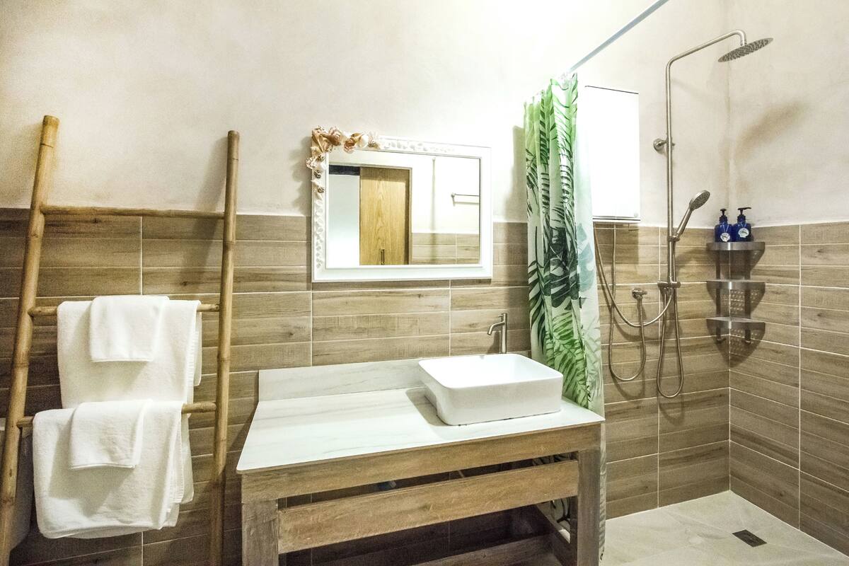 A bathroom with a wooden vanity, a white sink, a mirror with a decorative frame, a shower with a handheld showerhead, and a towel rack with white towels.