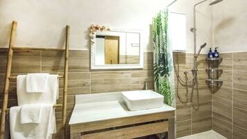 Une salle de bain avec un meuble-lavabo en bois, un lavabo blanc, un miroir avec un cadre décoratif, une douche équipée d’un pommeau de douche à main et un porte-serviettes avec des serviettes blanches.