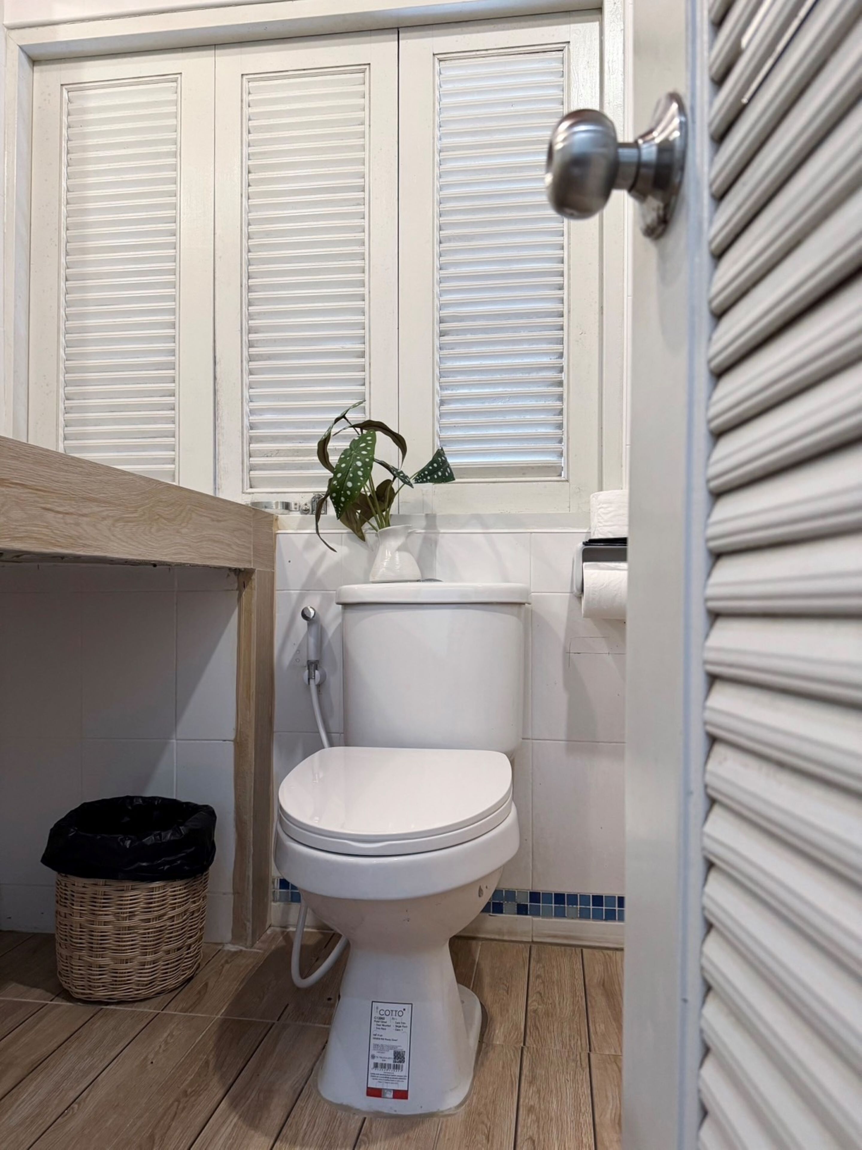 A bathroom with a toilet, a wicker basket, and a window with blinds.