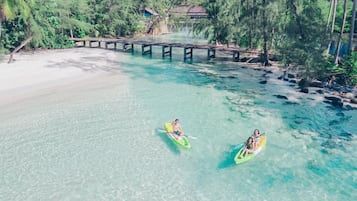 A clear view of a beach with kayaks in the water, a wooden bridge, and a building in the background.