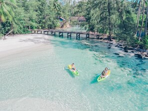 A clear view of a beach with kayaks in the water, a wooden bridge, and a building in the background. - A la Koh Kood (Ko Kood)