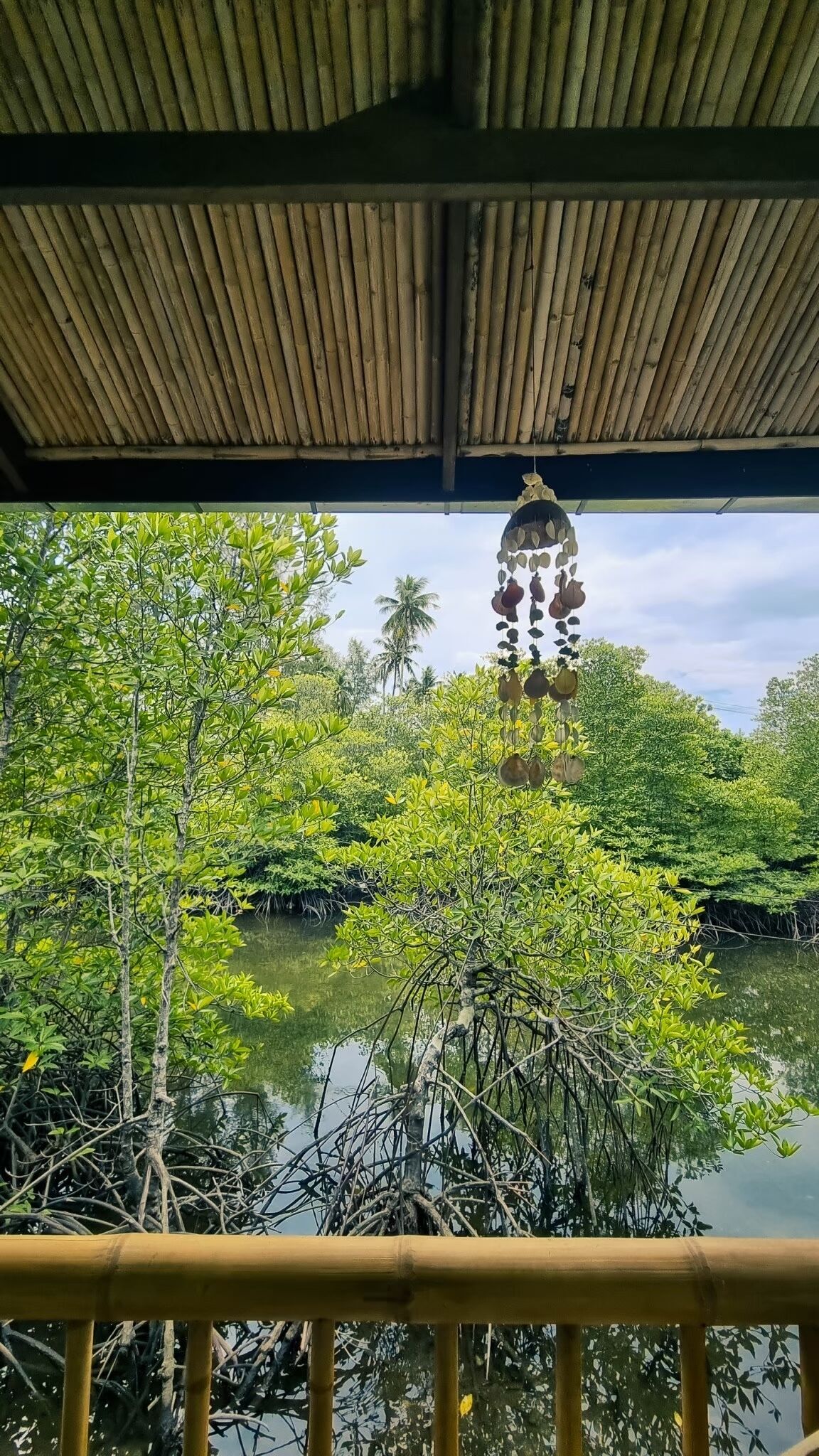 A bamboo structure with a hanging ornament, surrounded by lush greenery and a calm water body.