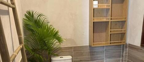 Une salle de bain avec des toilettes, une plante en pot, une échelle en bois et une étagère.