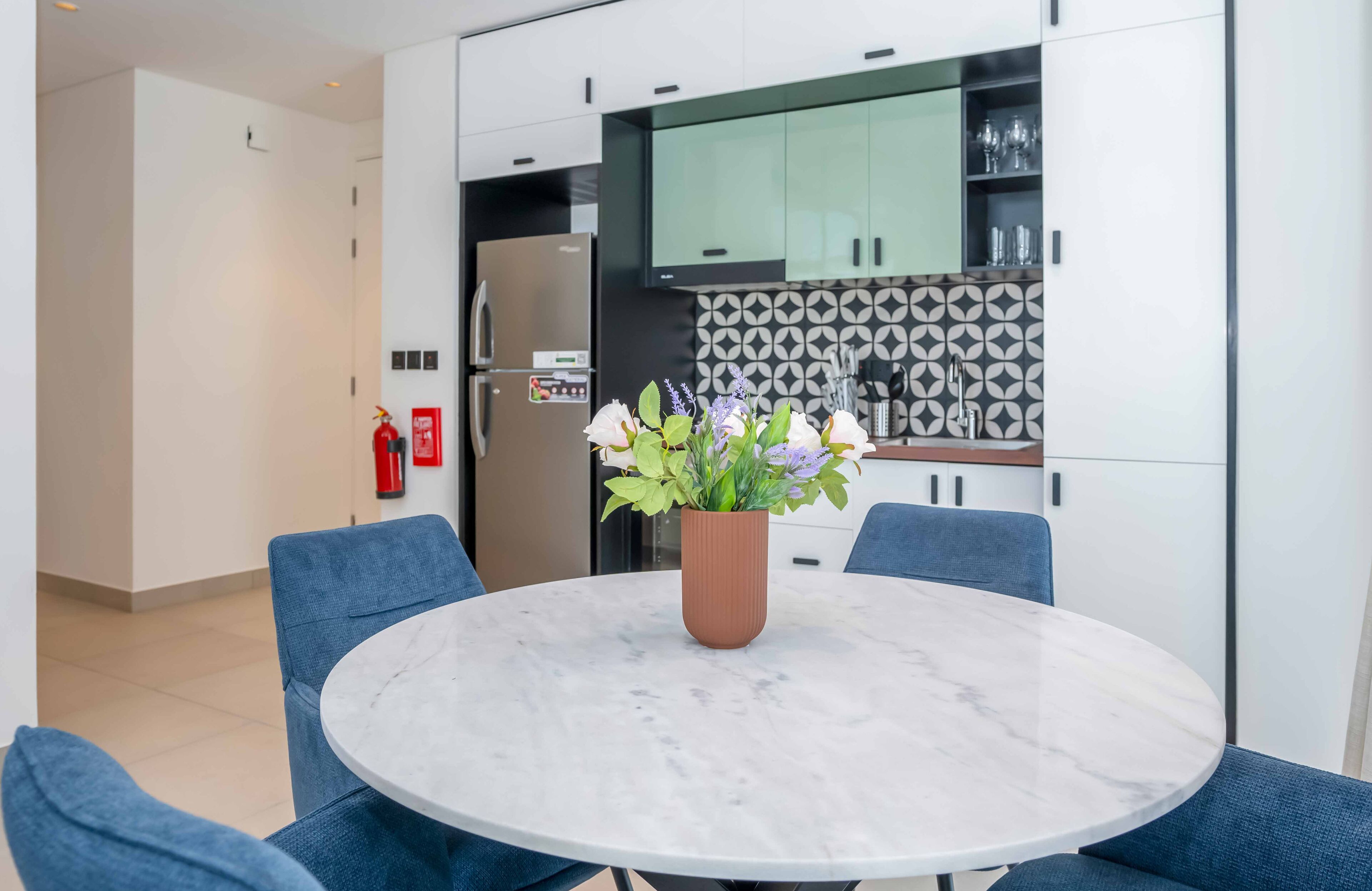 A modern kitchen with white cabinets, a marble countertop, and a potted plant.