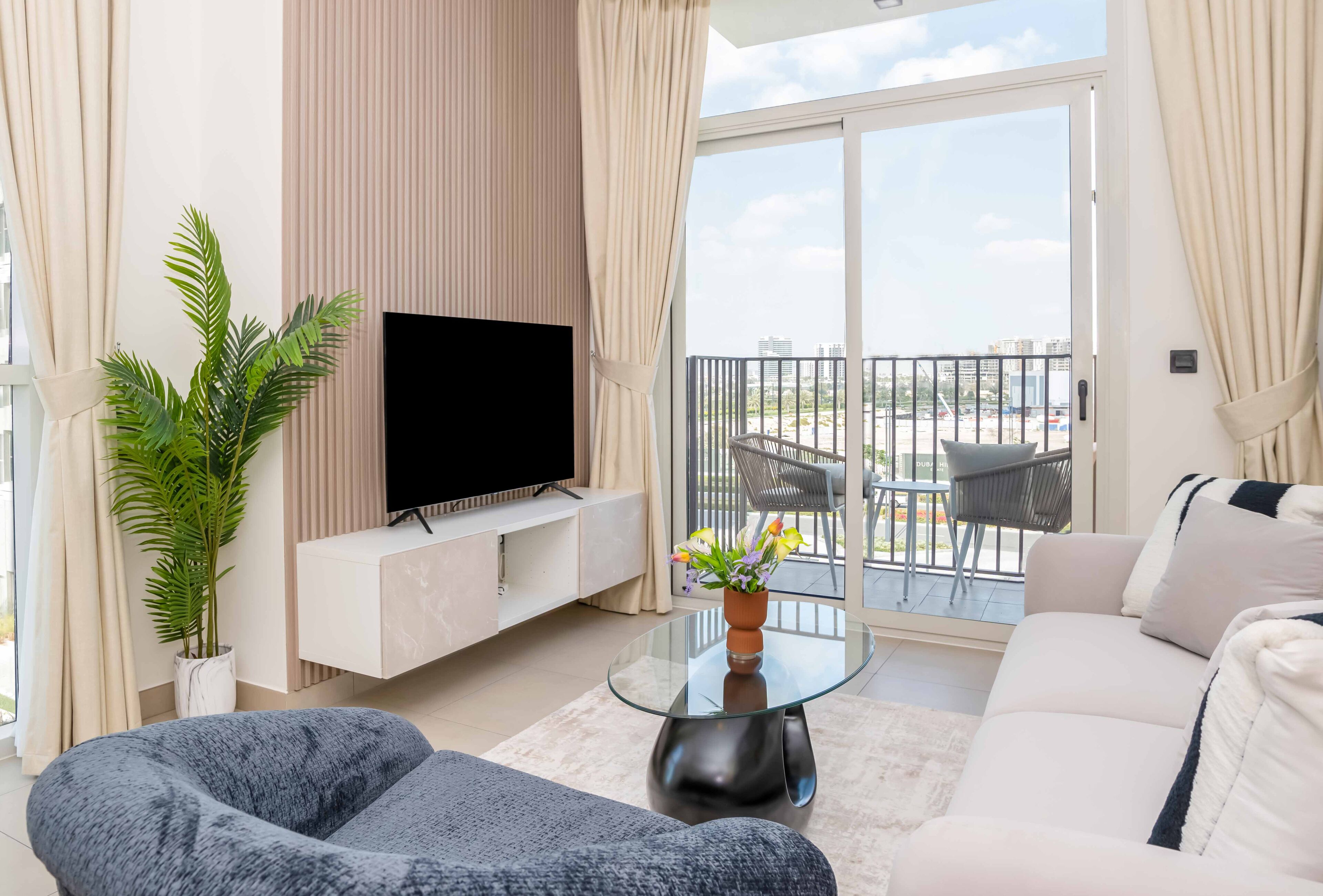 A modern living room with a flat-screen TV, a potted plant, and a glass coffee table.