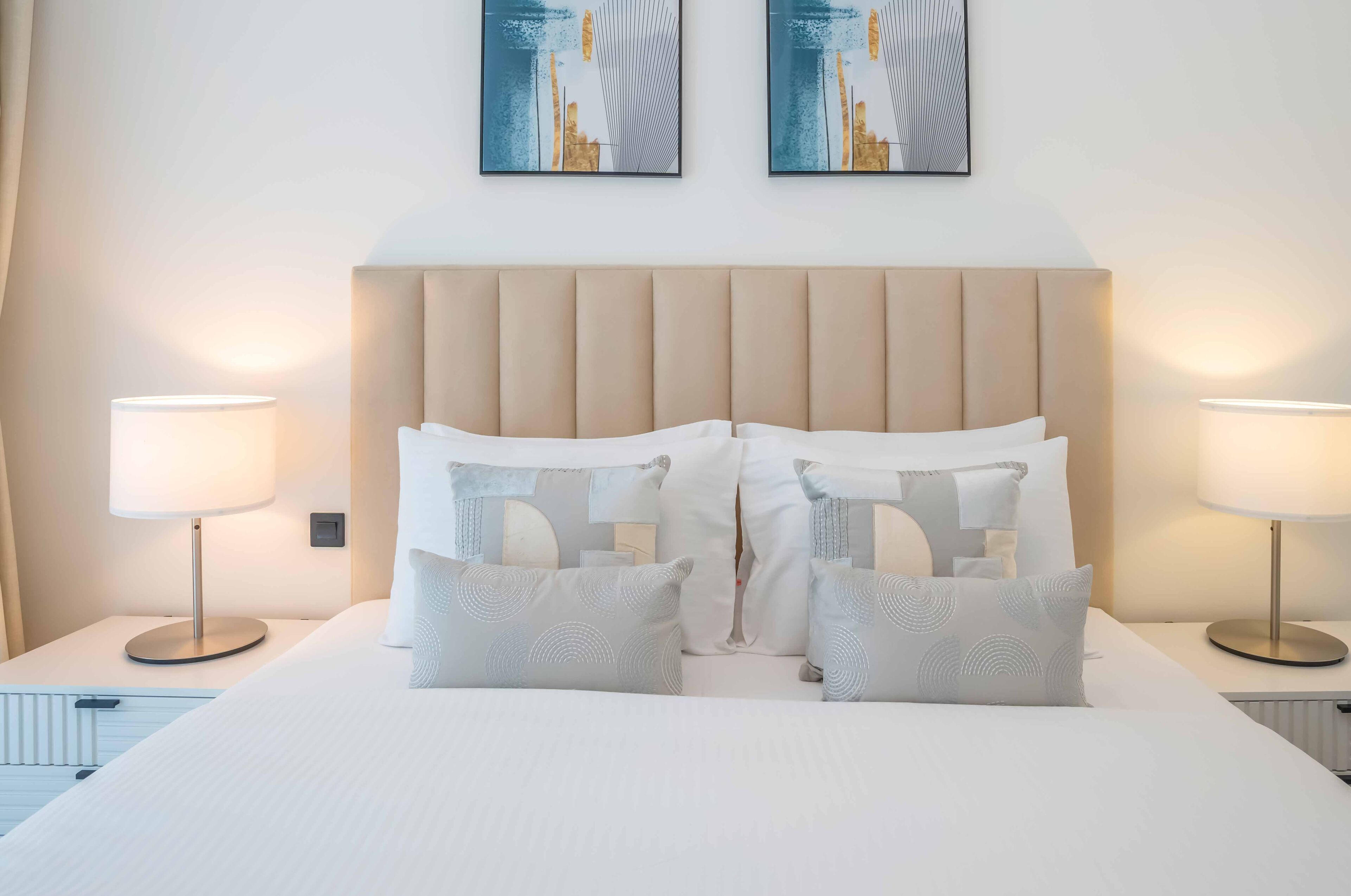 Une chambre d’hôtel avec un grand lit, deux lampes de chevet et deux œuvres d’art abstraites accrochées au mur.