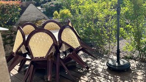 Eine Holzterrasse mit Tisch und Stühlen, umgeben von Grünpflanzen und einem Gebäude im Hintergrund.