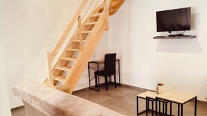 Ein modernes Wohnzimmer mit einer Couch, einer Holztreppe, einem an der Wand befestigten Fernseher und einem kleinen Tisch.