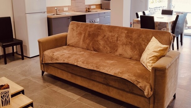 Ein Wohnzimmer mit einer Couch, einem kleinen Tisch, einer Küchenzeile mit Kühlschrank und einem Essbereich mit Stühlen.