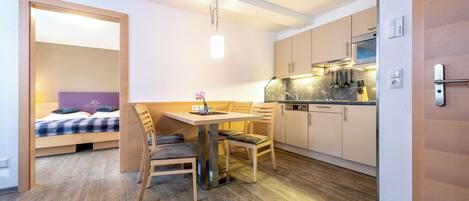 Una habitación de hotel compacta con kitchenette, un comedor con mesa y sillas, y una cama con cabecera morada.