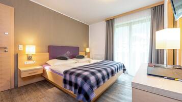 A modern hotel room with a large bed, bedside lamps, a wooden nightstand, a desk with a lamp, and a view of the outdoors through the window.