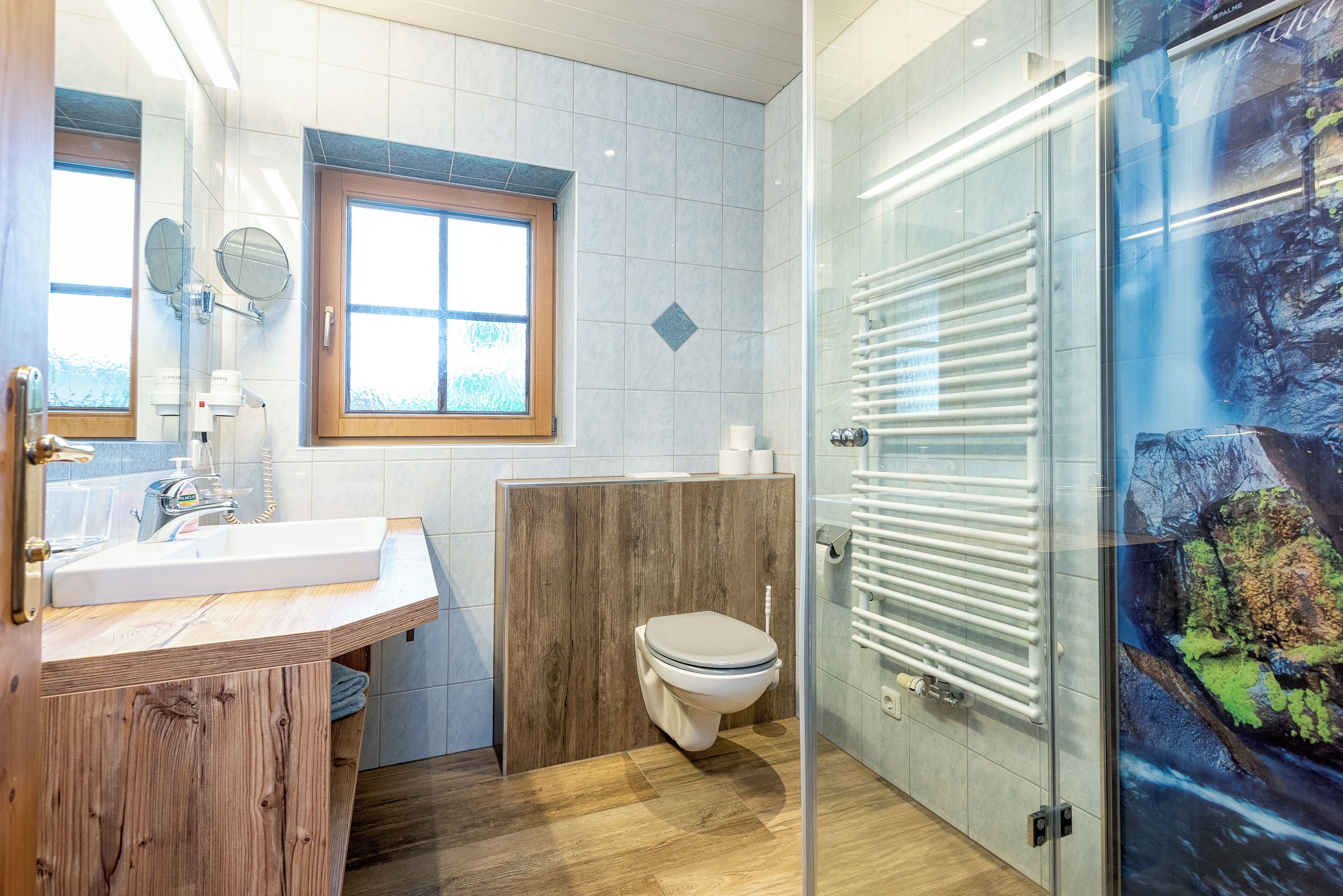 Un baño con tocador de madera, inodoro, ventana y cabina de ducha de vidrio.