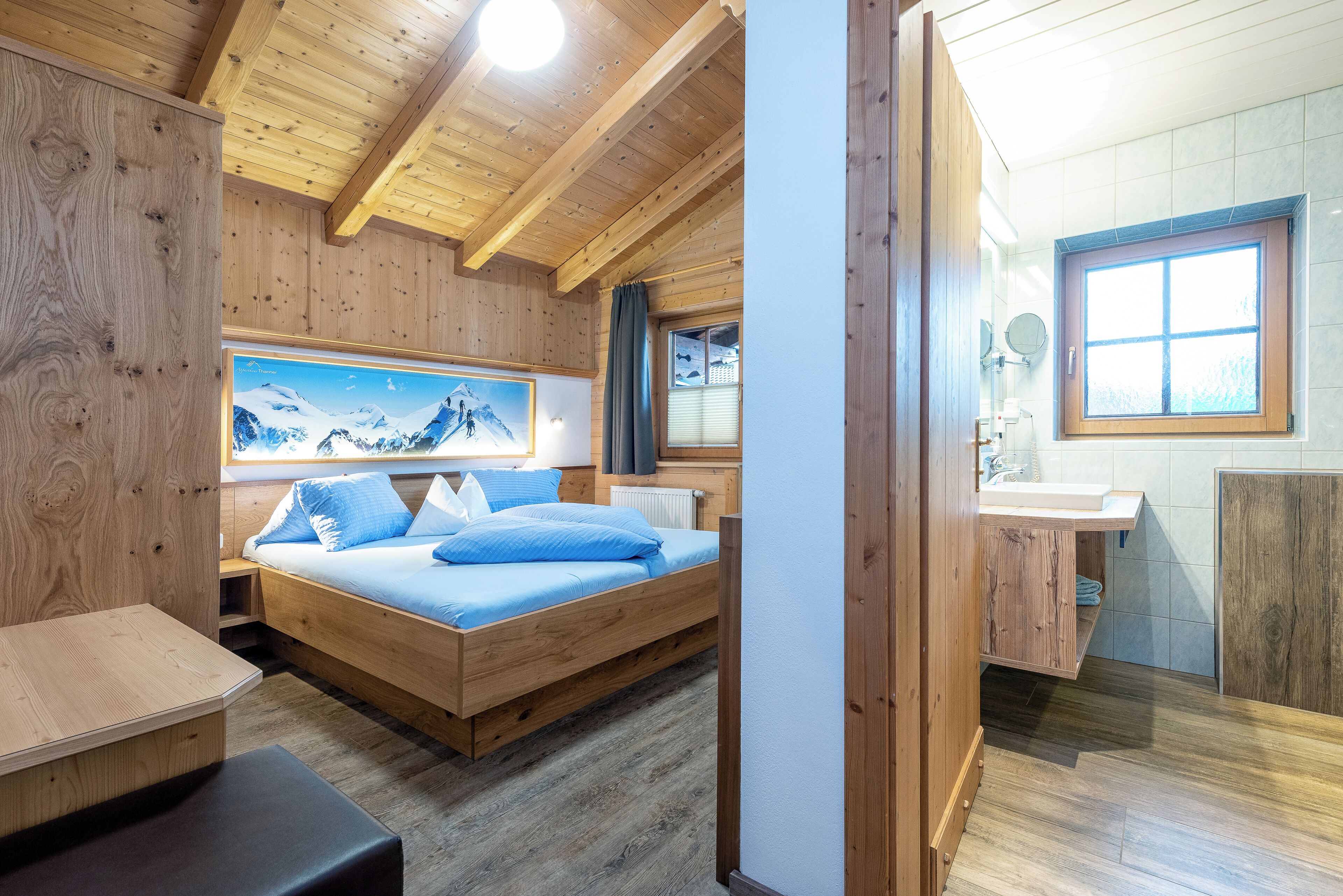 A wooden cabin room with a bed, a large window, and a bathroom with a wooden cabinet.