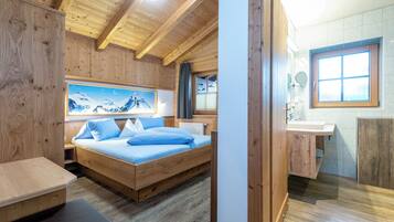 A wooden cabin room with a bed, a large window, and a bathroom with a wooden cabinet.