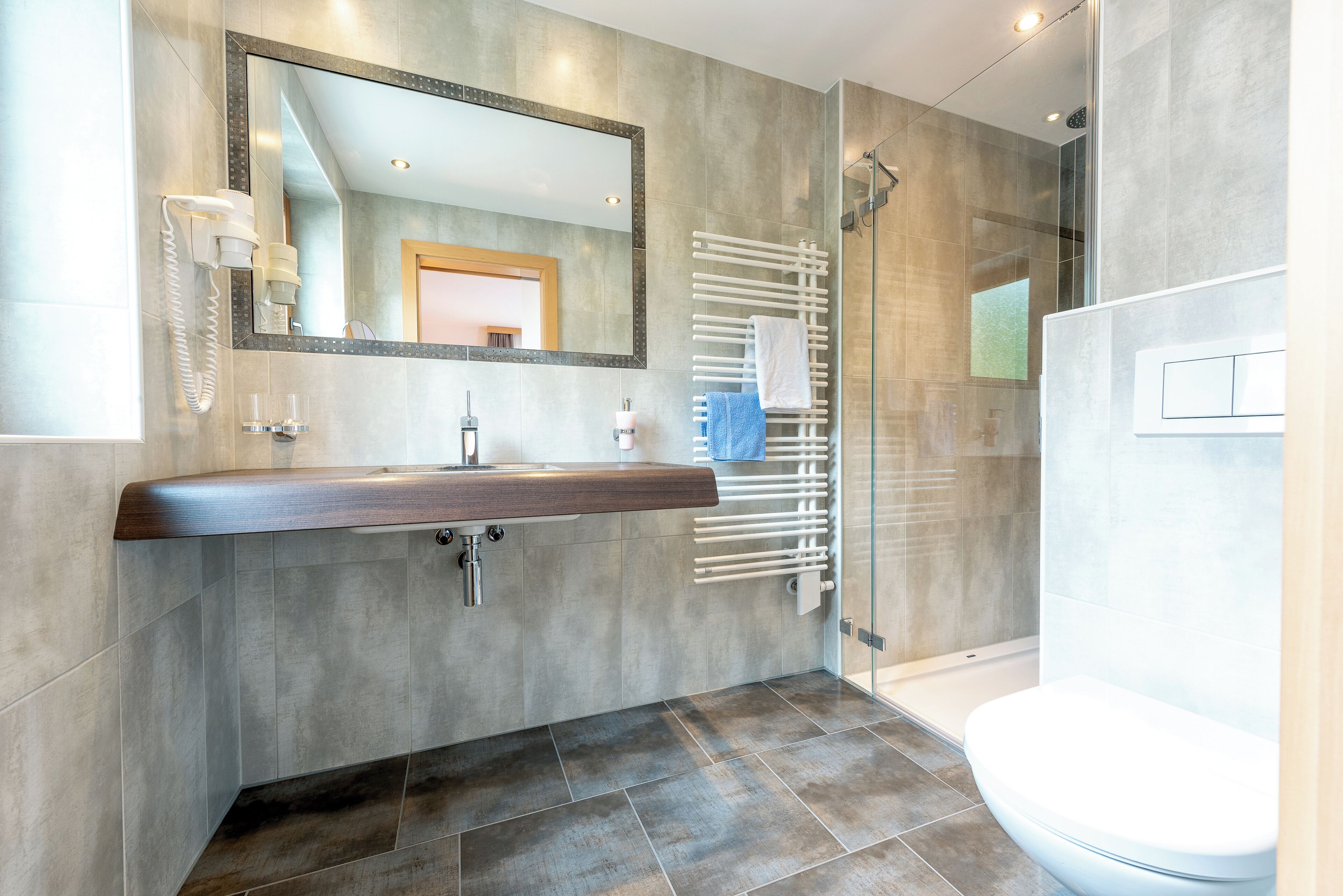 Une salle de bain moderne avec un grand miroir, un meuble-lavabo en bois, une cabine de douche en verre et des toilettes blanches.