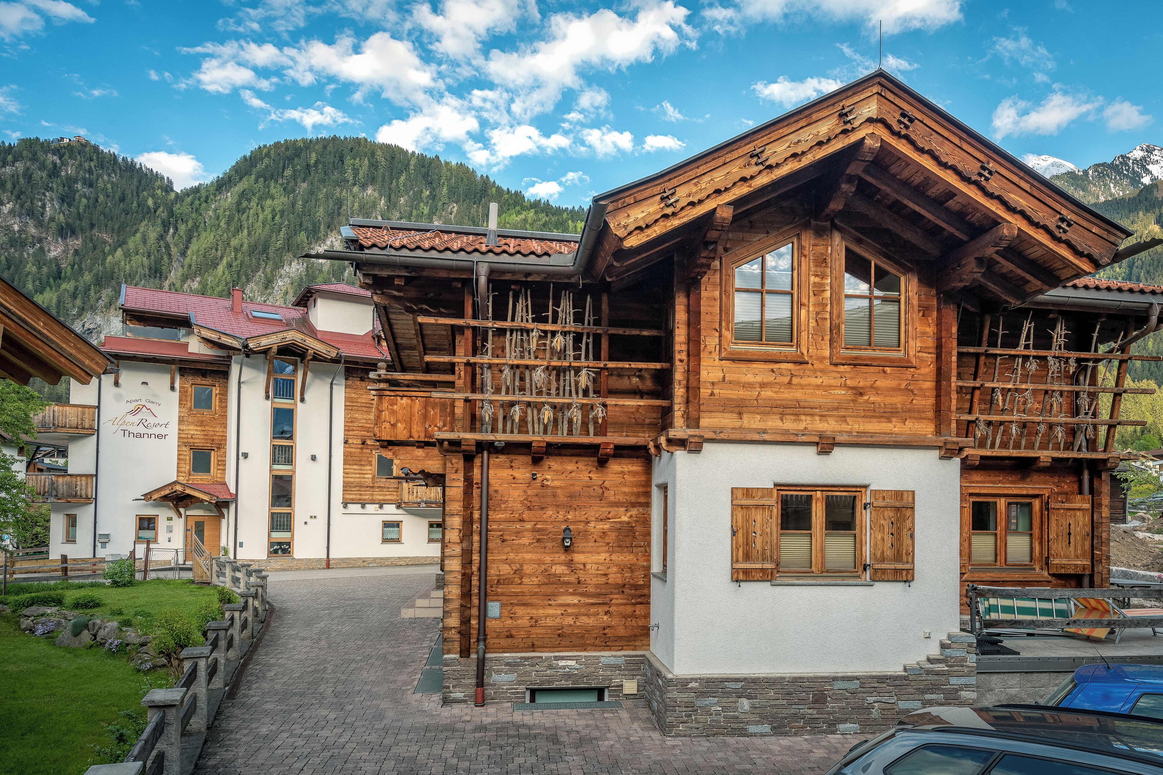 A wooden chalet with a balcony, a stone staircase, and a mountain backdrop.