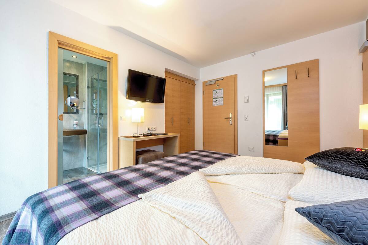A hotel room with a bed, a desk, a TV, and a shower area.