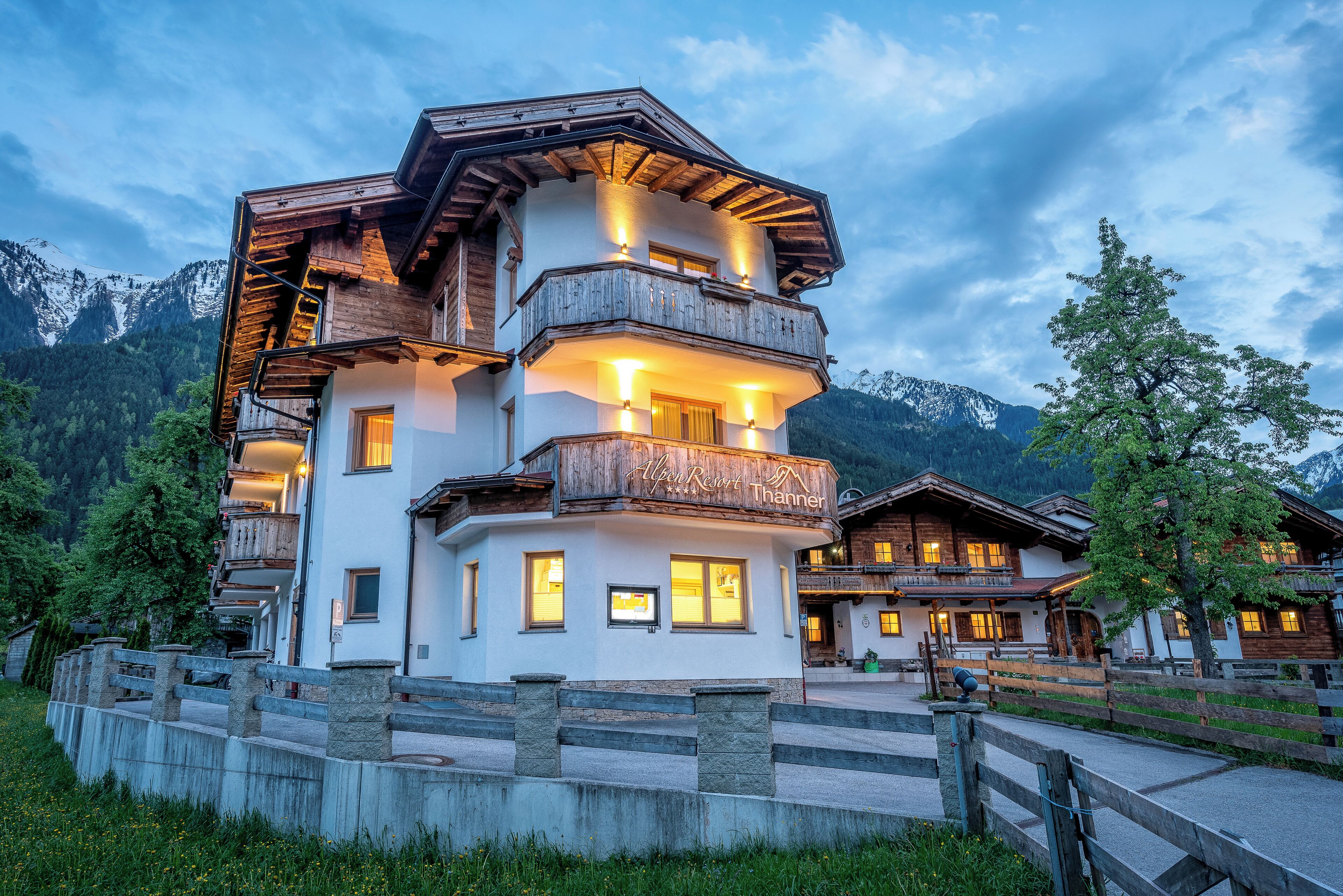 Ein mehrstöckiges Hotel mit Balkonen, einer Steinmauer und einem Bergpanorama im Hintergrund.