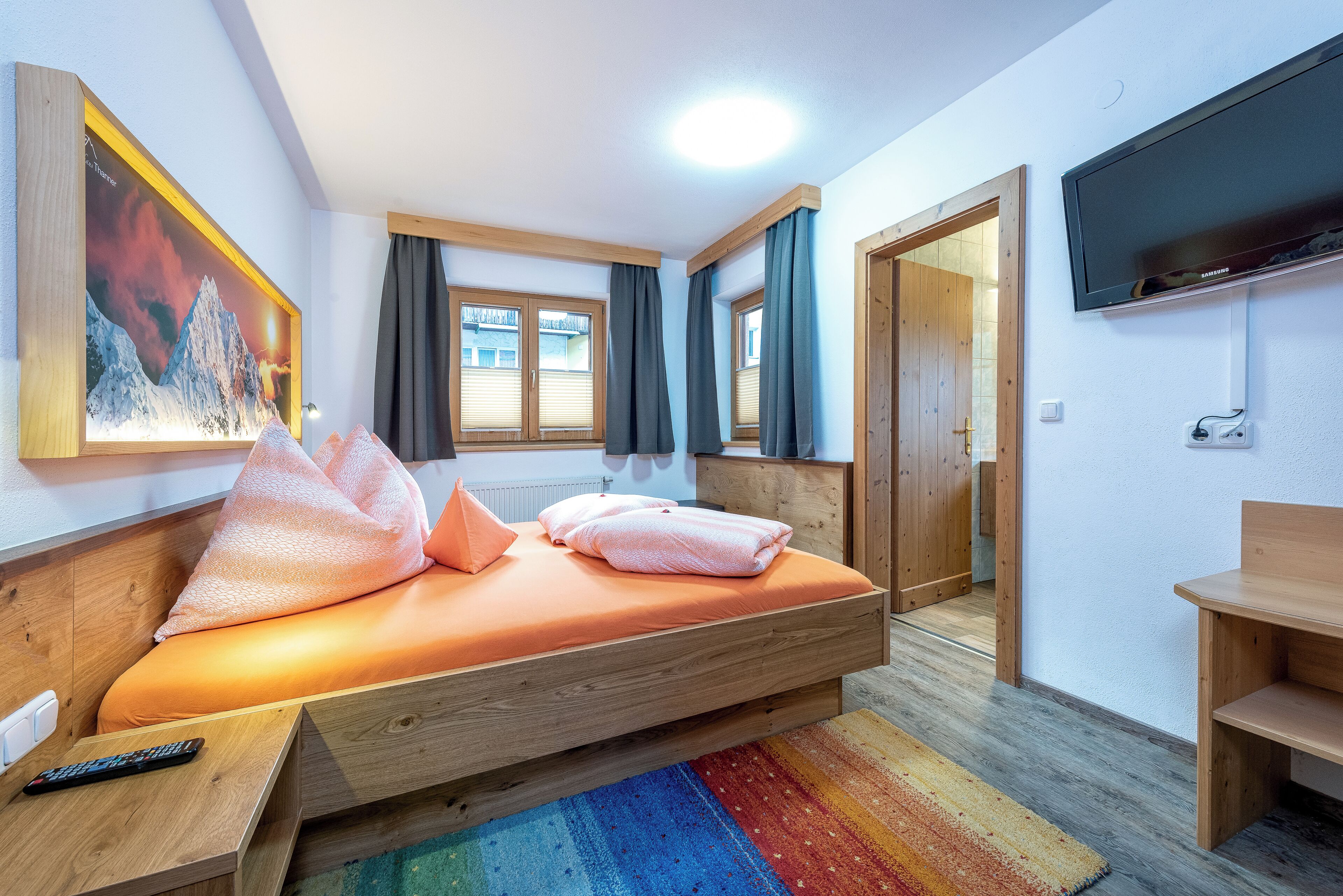 A bedroom with a bed, a TV, a painting, and a window.