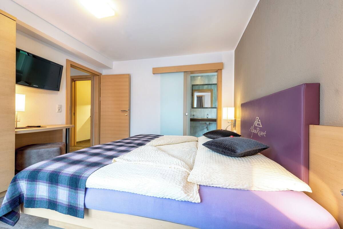 A hotel room with a bed, a TV mounted on the wall, a desk, and a mirror.