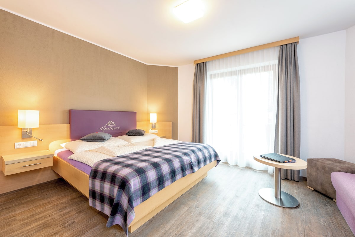 A modern hotel room with a bed, bedside tables, a small round table, and a sofa.